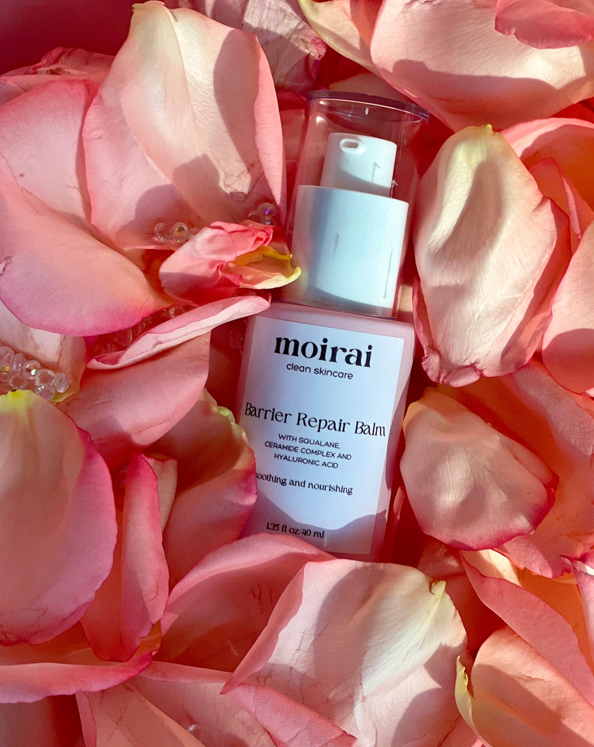 Moirai Barrier Repair Balm pump bottle nested among pink rose petals in warm light.