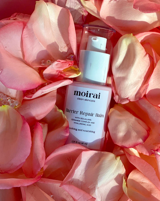 Moirai Barrier Repair Balm pump bottle nested among pink rose petals in warm light.