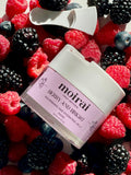 A jar of 'Berry and Bright Face Mask' by Moirai Skincare placed among an array of fresh berries, including raspberries, blueberries, and blackberries.
