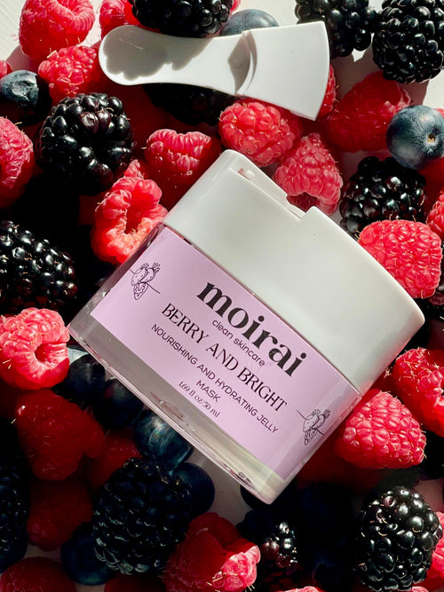 A jar of 'Berry and Bright Face Mask' by Moirai Skincare placed among an array of fresh berries, including raspberries, blueberries, and blackberries.