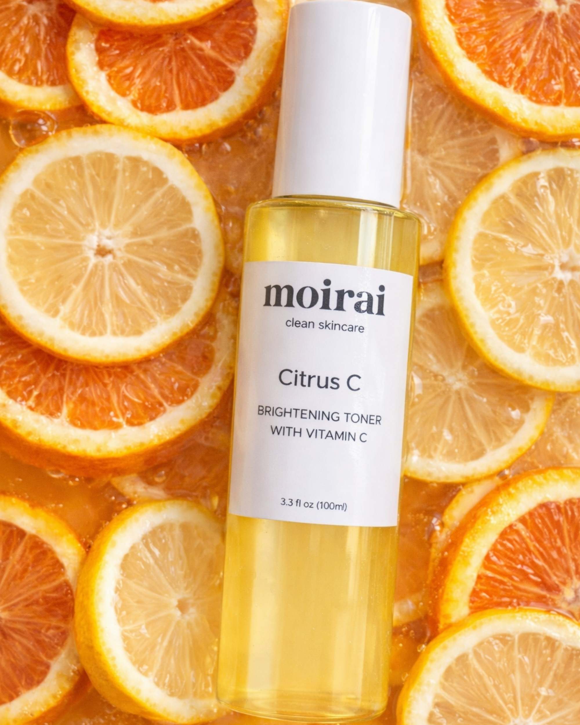Moirai Citrus C Brightening Toner with Vitamin C in a clear yellow bottle surrounded by fresh orange and lemon slices