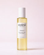 Moirai Citrus C Brightening Toner with Vitamin C in a clear yellow bottle on a soft blush background