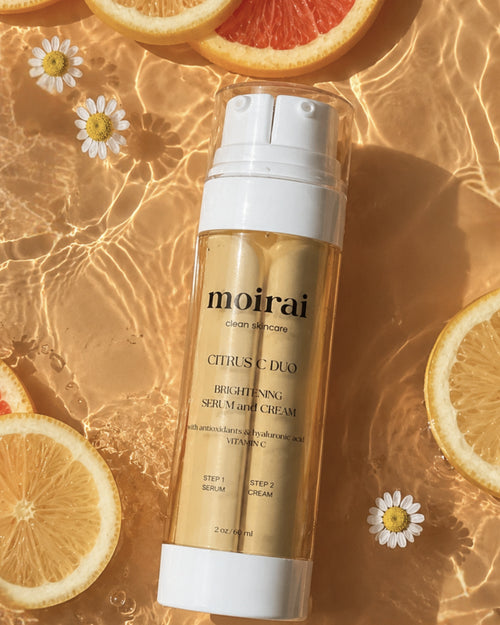 Moirai Citrus C Duo brightening vitamin C serum and cream in one bottle with the dual-delivery system  surrounded by fresh citrus slices and water 
