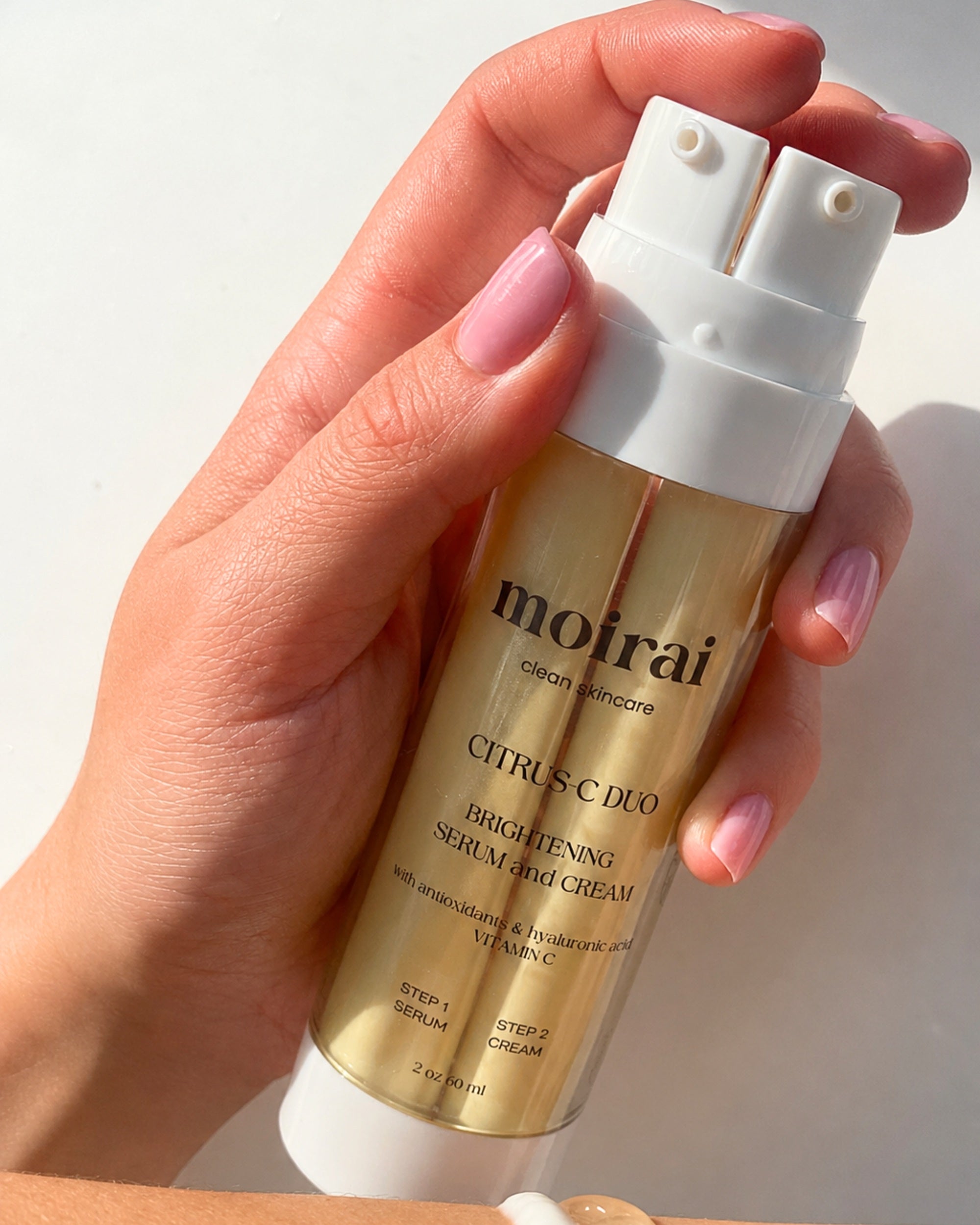 Moirai Citrus C Duo brightening serum and cream in one bottle with vitamin C, antioxidants and hyaluronic    acid held in hand with visible serum and cream texture.