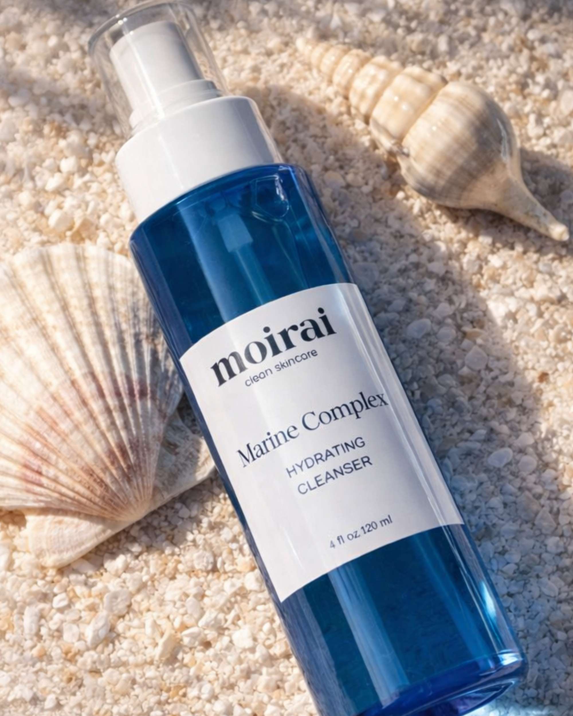 Moirai Marine Complex Hydrating Cleanser blue bottle with seashells on sand
