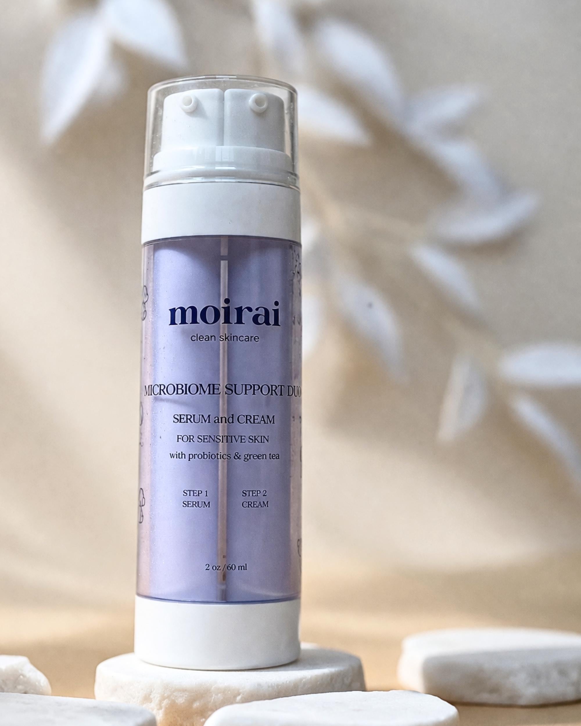 Moirai Microbiome Support Duo Serum and Cream in a lavender dual-chamber bottle on white stones with a soft neutral background.