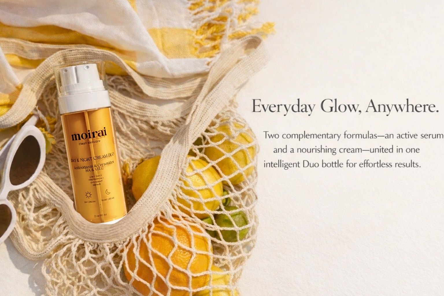 Moirai Duo dual-delivery Day and Night cream skincare bottle styled with citrus fruits in a mesh tote.